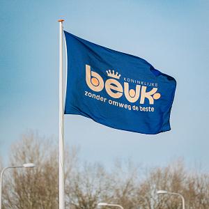 Blauwe Beuk-vlag met logo en slogan wapperend aan vlaggenmast tegen heldere lucht