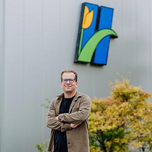 Man die buiten poseert voor het pand van Heemskerk Flowers, met het opvallende tulpenlogo groot zichtbaar op de gevel.
