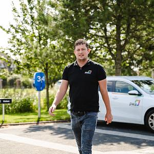 PWA-medewerker loopt over parkeerterrein bij kantoor in Noordwijkerhout met PWA-bedrijfsauto op de achtergrond.