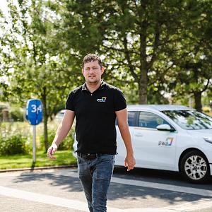 PWA-medewerker loopt over parkeerterrein bij kantoor in Noordwijkerhout met PWA-bedrijfsauto op de achtergrond.