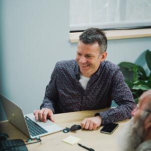Overleg tussen collega’s aan tafel waarbij samen wordt gewerkt op een laptop in een informele setting.