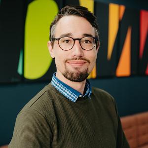 Medewerker van PWA poseert in een modern ingerichte kantoorruimte met kleurrijke wanddecoratie en een informele sfeer.
