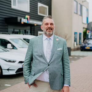 Man in PWA-bedrijfskleding loopt over een parkeerterrein met een PWA-auto en groene omgeving op de achtergrond.