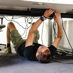 PWA-medewerker werkt kabels weg onder een bureau tijdens de installatie van een IT-werkplek.