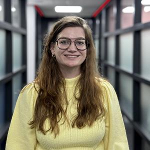 Vriendelijke medewerker poseert in een moderne kantooromgeving met glazen wanden en strakke verlichting.