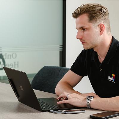 PWA-medewerker werkt geconcentreerd achter een laptop aan een vergadertafel, met telefoon en sleutels naast zich.