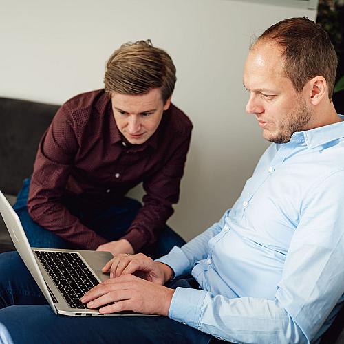Twee collega’s bekijken samen een laptop tijdens een overleg in een kantoorruimte.