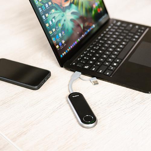 Laptop op een bureau met een aangesloten Yealink USB-adapter en een smartphone ernaast.