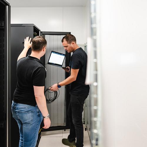 2 personen met PWA shirt, staand voor een serverkast. 1 persoon met een netwerkkabel en laptop in hand.