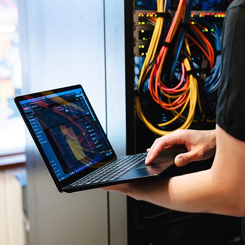 IT-specialist van PWA werkt met laptop in serverruimte met netwerkbekabeling.