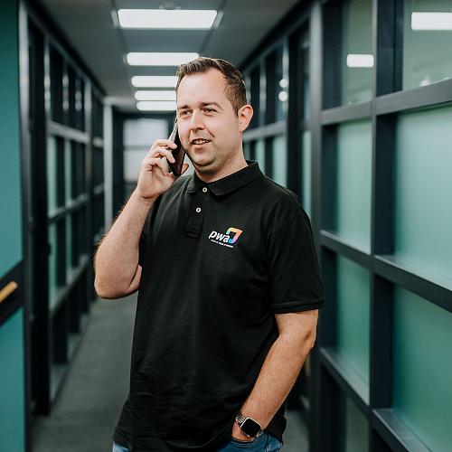 PWA-medewerker voert een telefoongesprek in de gang van het kantoor, gekleed in een PWA-polo.