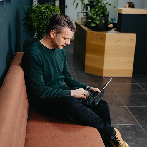 PWA-medewerker werkt met laptop op een bank in de ontvangstruimte.