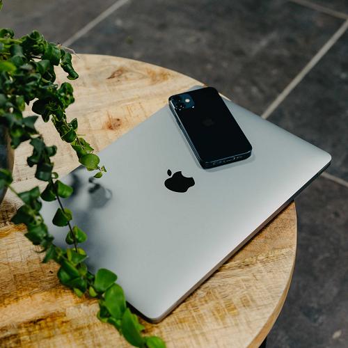 MacBook met iPhone op een houten tafel naast een groene plant, symbool voor moderne werkplek en technologie.