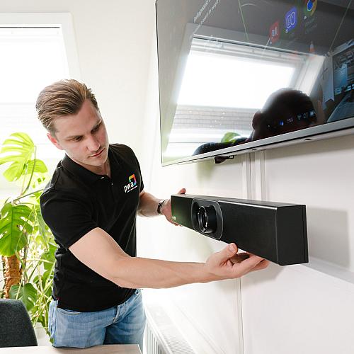 PWA-medewerker monteert een videobar onder een scherm in een vergaderruimte.