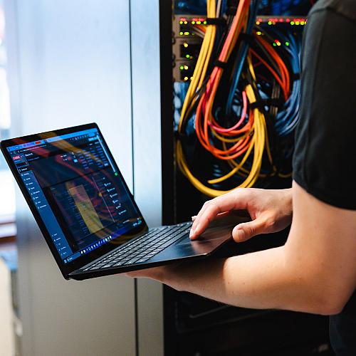 PWA-medewerker controleert netwerkapparatuur met laptop bij serverkast met netwerkkabels.