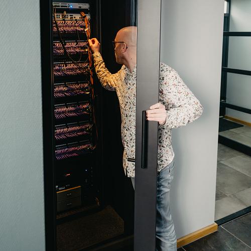 IT-specialist werkt aan een serverrack in een moderne kantooromgeving, met focus op netwerkbeheer en technische infrastructuur.