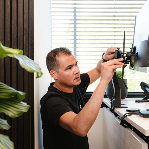 IT-specialist installeert een monitor op een moderne werkplek, met oog voor ergonomie en gebruiksgemak.