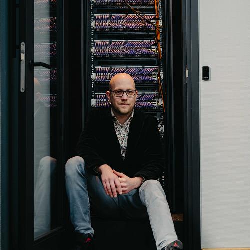 IT-specialist van PWA zit ontspannen voor een volledig bekabeld serverrack in een moderne technische ruimte.