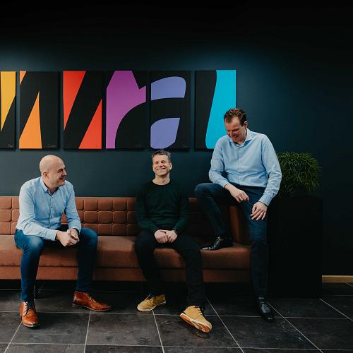 3 mannen op een bank met een kleurrijk schilderij erboven