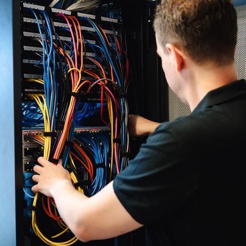 Lachende man staat achter een bureau en werkt op een computer in een moderne kantooromgeving, bezig met een schroevendraaier en een laptop.