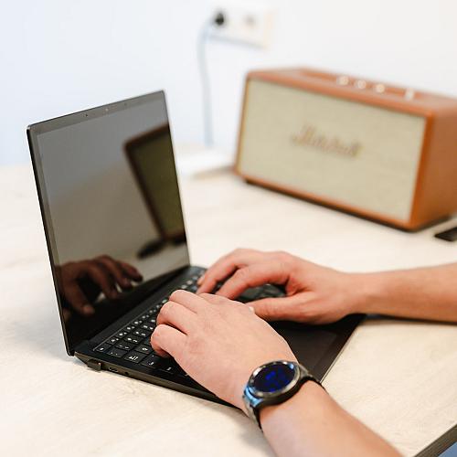 Een persoon typt op een laptop aan een lichtgekleurde tafel, met een Marshall speaker op de achtergrond.