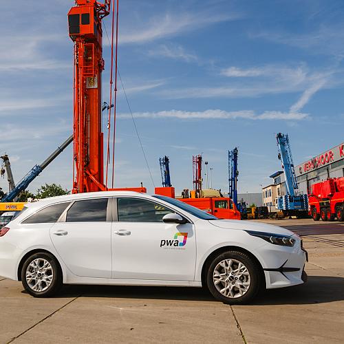 Witte auto met PWA-bestickering op de voorgrond met hijskranen op de achtergrond.