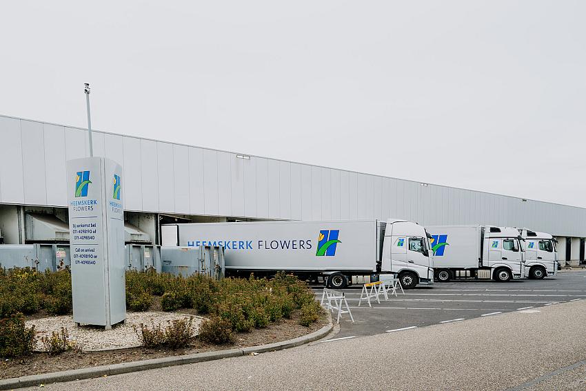 Vrachtwagens van Heemskerk Flowers opgesteld bij het distributiecentrum, met het bedrijfslogo zichtbaar op trucks en zuil voor het gebouw.