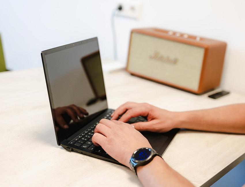 Man typt op een laptop aan een licht bureau, met een Marshall speaker en een smartwatch zichtbaar in beeld.