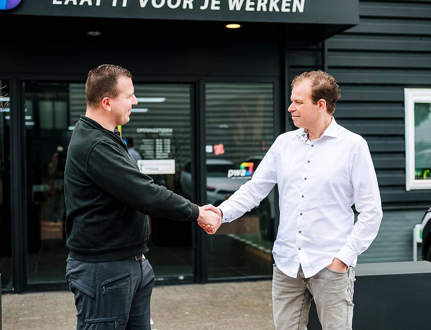 Twee mannen schudden elkaar de hand voor de entree van het PWA-pand, als symbool voor samenwerking en klantcontact.