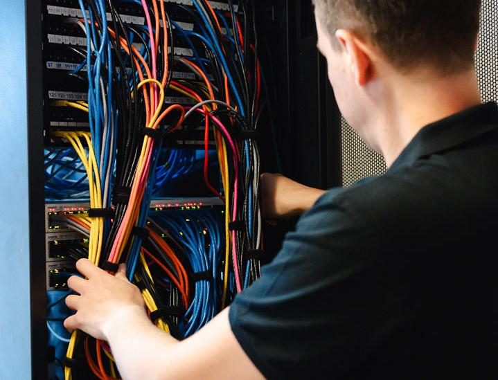 IT-specialist werkt aan een patchkast vol gekleurde netwerkkabels in een serverruimte.