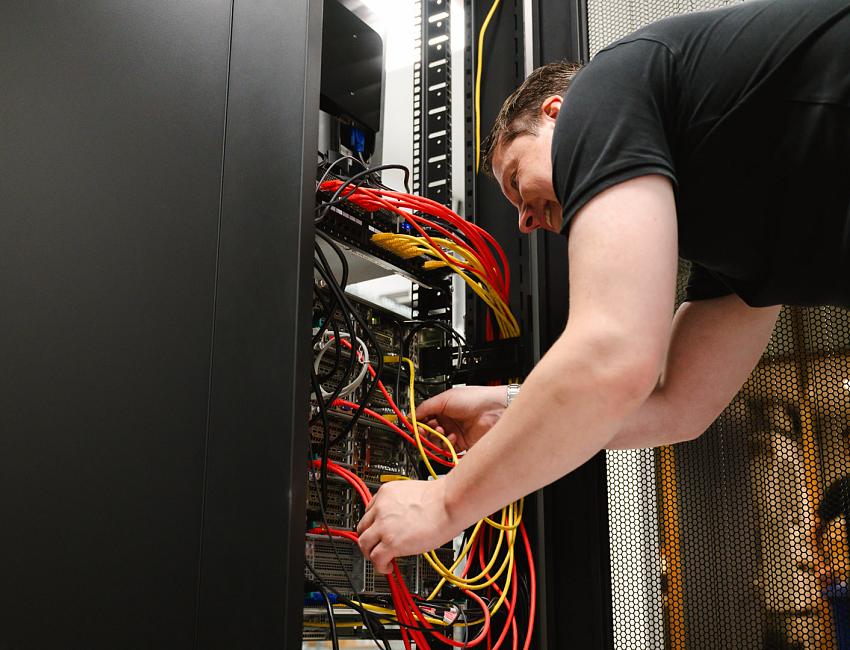 Man werkt geconcentreerd aan een serverkast en sluit kleurrijke netwerkkabels aan in een technische ruimte.