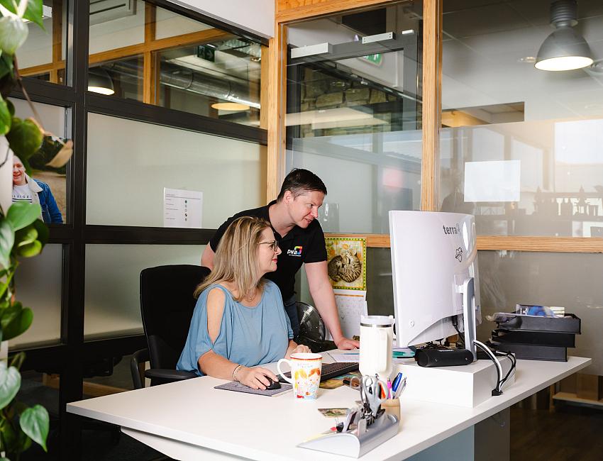 PWA-collega’s werken samen aan een bureau en bekijken informatie op een beeldscherm in een open kantooromgeving.