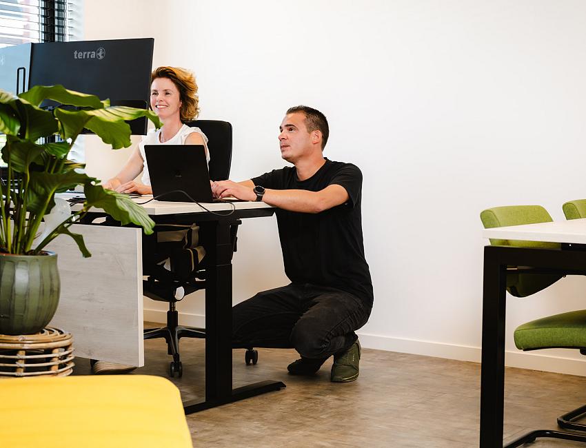 Collega’s werken samen aan een bureau met laptop in een moderne kantoorruimte.