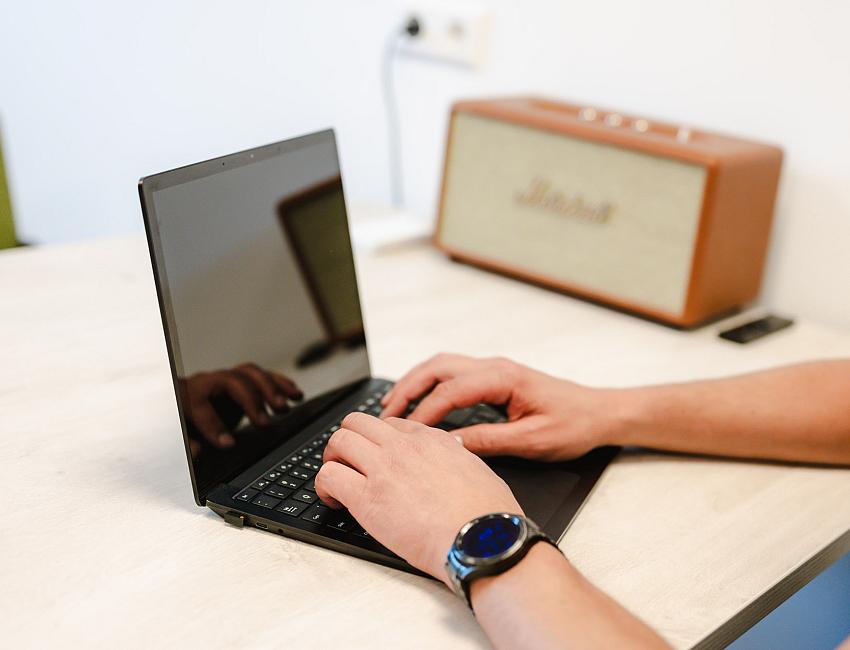 Handen die typen op een zwarte laptop op een bureau, met op de achtergrond een Marshall speaker.