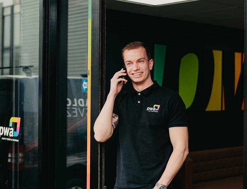 Lachende man werkt aan een computer in een kantoorruimte met grijze schermwanden en een houten bureau.