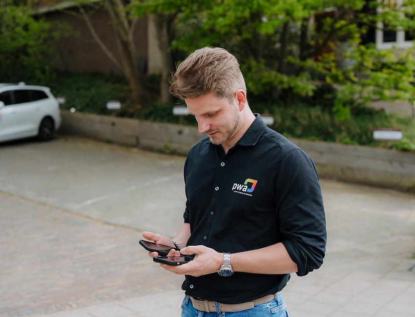 PWA-medewerker gebruikt een smartphone buiten bij een klant tijdens een bezoek voor IT-beheer.