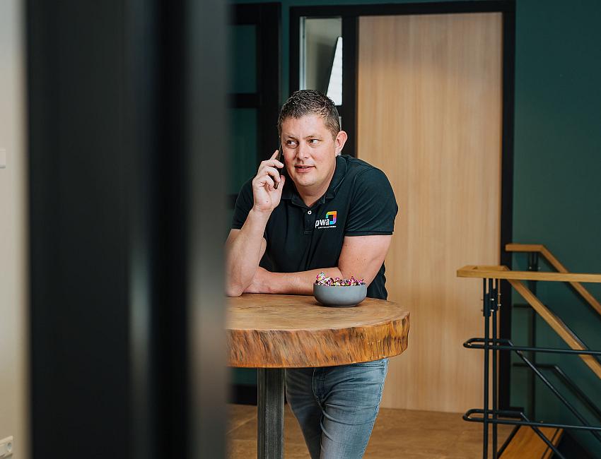 IT-consultant belt aan een statafel in een kantooromgeving.