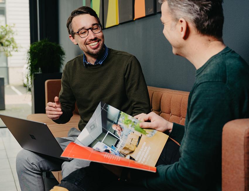 2 mannen op bank die samen kijken naar een laptop.