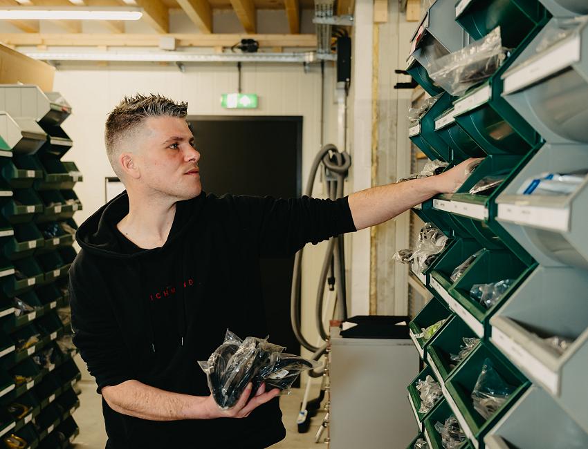 PWA-medewerker pakt onderdelen uit het magazijn, te midden van overzichtelijk gesorteerde IT-materialen.